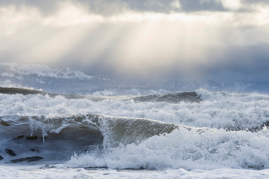 Rough waves along a beach in Homer in Winter with sun rays overhead, Kachemak Bay, Kenai Peninsula, Southcentral Alaska