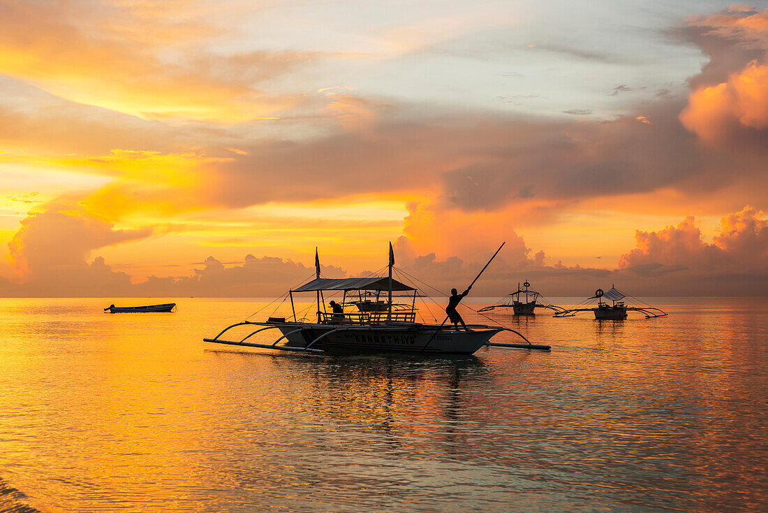 Beautiful sunrise in Alona Beach, a man moving his boat to reach the shore with a long stick, Panglao Island, Bohol, Philippines