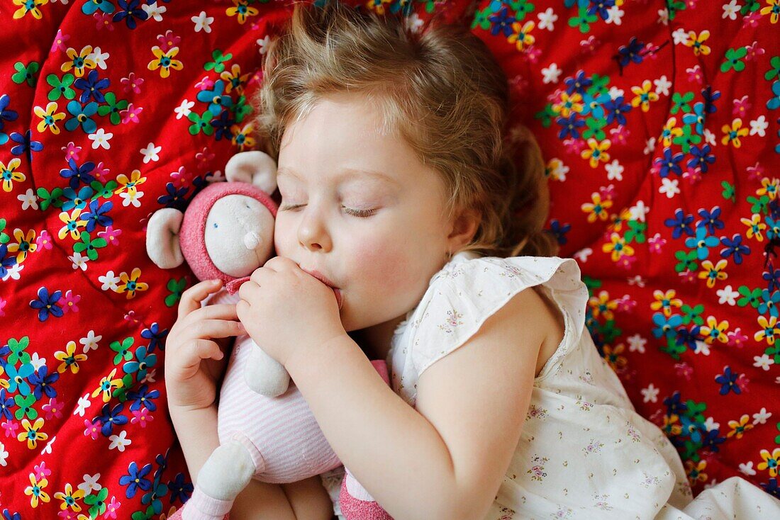 A 3 years old girl sleeping and sucking his thumb, lying on her bed