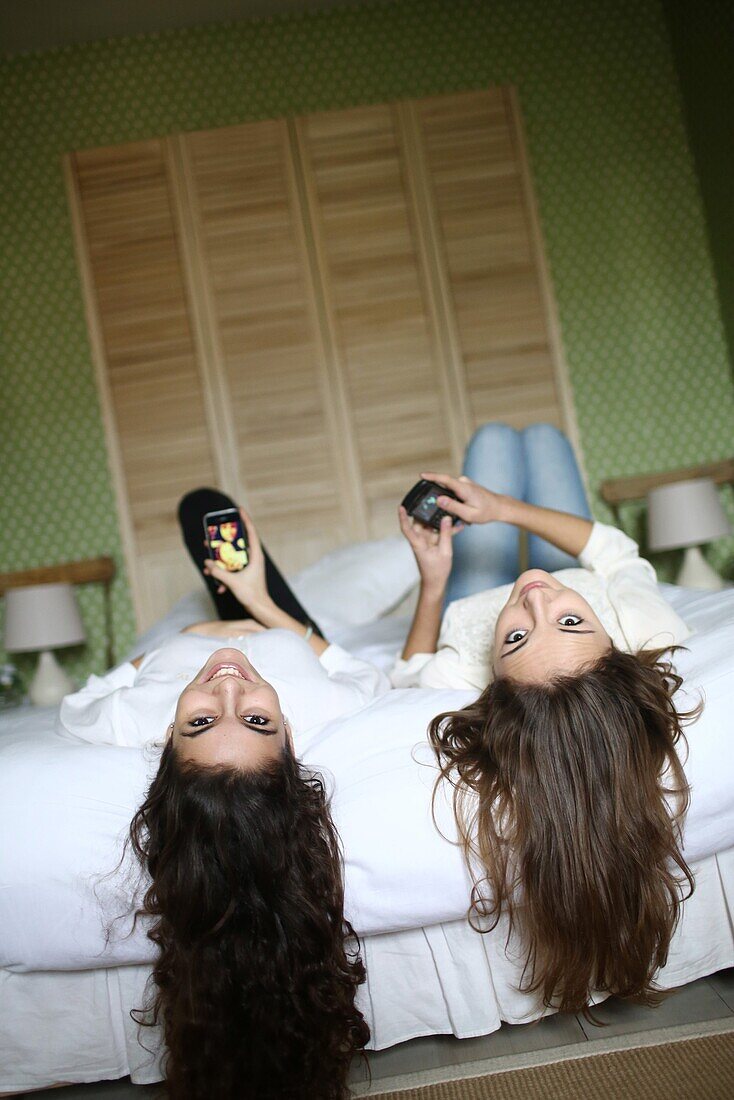 2 teens playing with their mobile phone on a bed