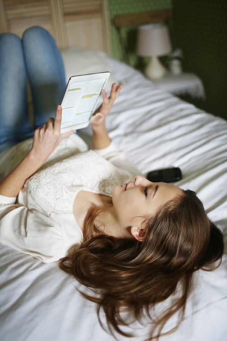 A teenage girl reading on a touch pad on her bed