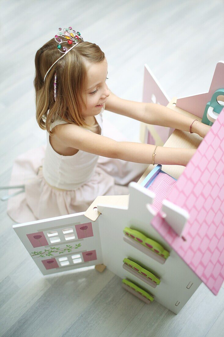 A 5 years old girl dressed like a princess playing with her dollhouse