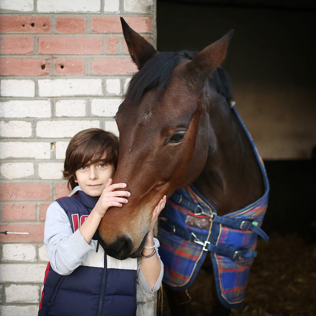 A boy stroking a horse in a stable