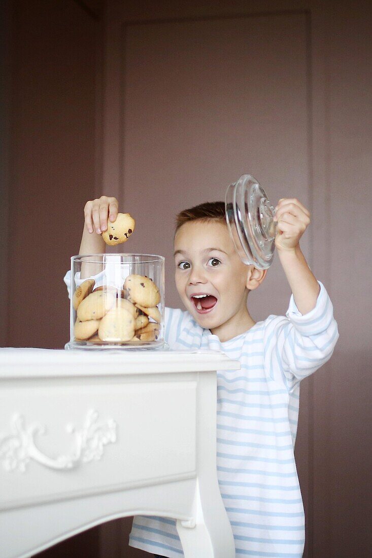 A little boy taking some cookies in a jar