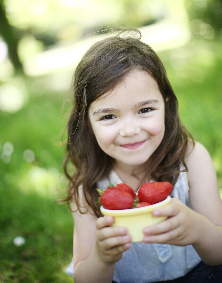 A 5 years old girl eating  strawberries in the countryside