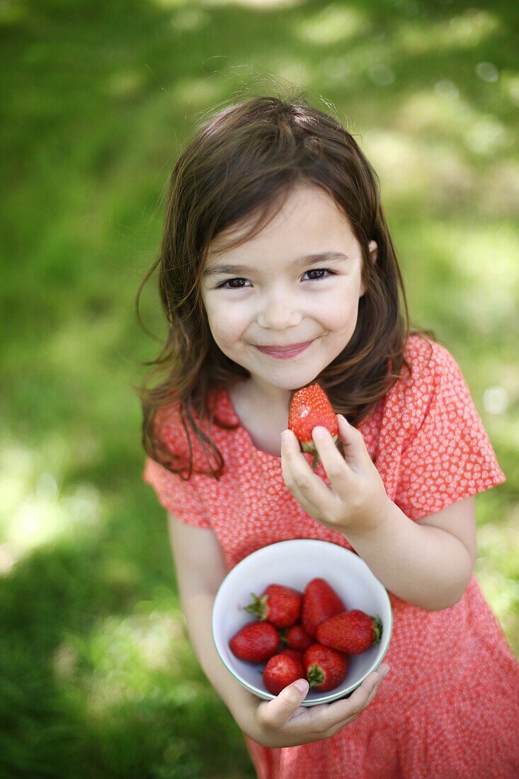 A 5 years old girl eating  strawberries in the countryside