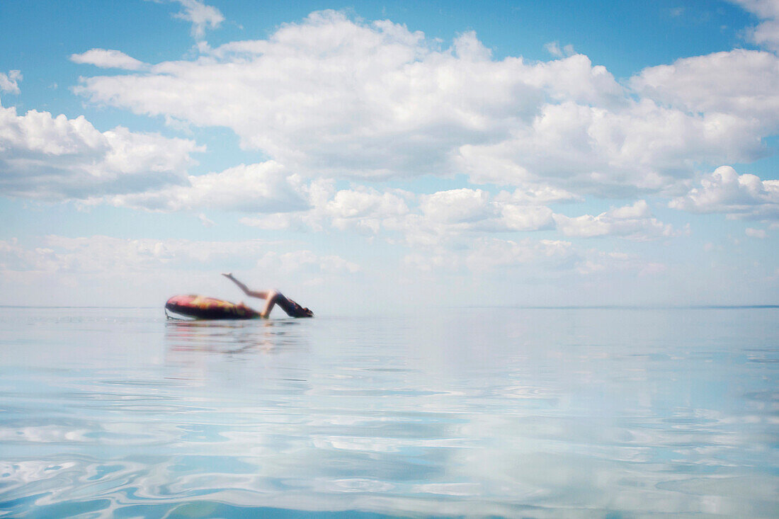 Caucasian teenage girl jumping from inner tube into lake