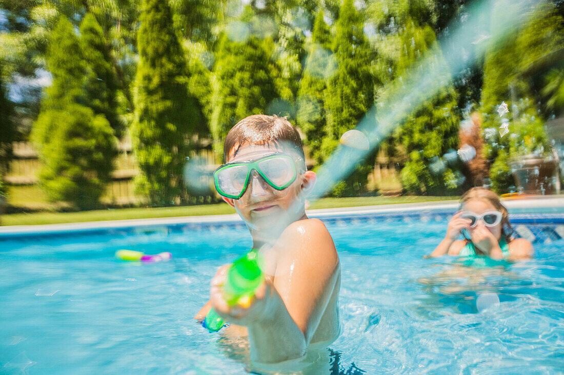 Caucasian boy playing with squirt gun in swimming pool