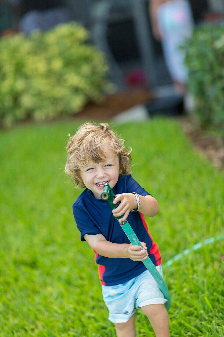 Caucasian baby boy playing with hose in backyard