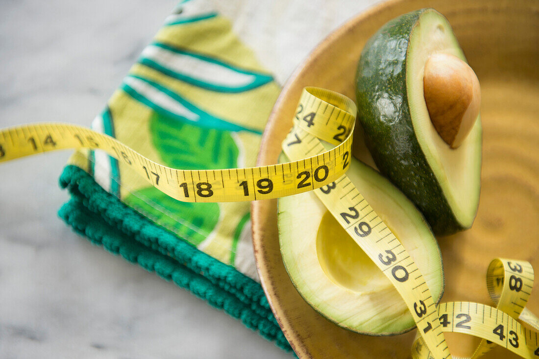 Close up of halved avocado, measuring tape and napkin on plate