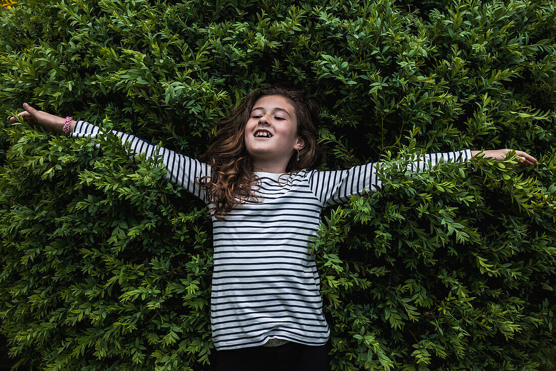 Portrait of Young Girl Extending Arms in Front of Shrub