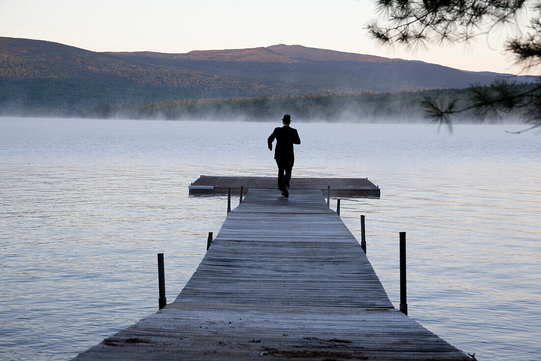 Businessman in Suit and Hat Running Down Lakeside Dock