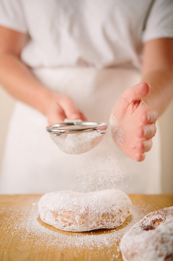 Woman Sprinkling Powdered Sugar on Doughnuts
