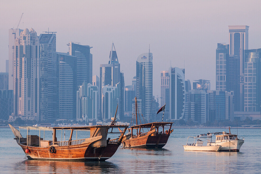 contrast between the traditional boats or qatari dhows at dock and the modern buildings in the skyline of the west bay city center, doha, qatar, persian gulf, middle east