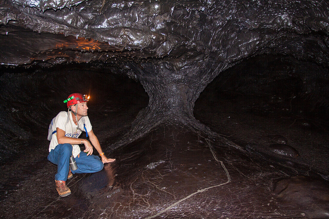 spelunking guide from the ricaric company admiring the geological formations in a lava tunnel running under the slopes of the piton de la fournaise (peak of the furnace), reunion island, indian ocean, france