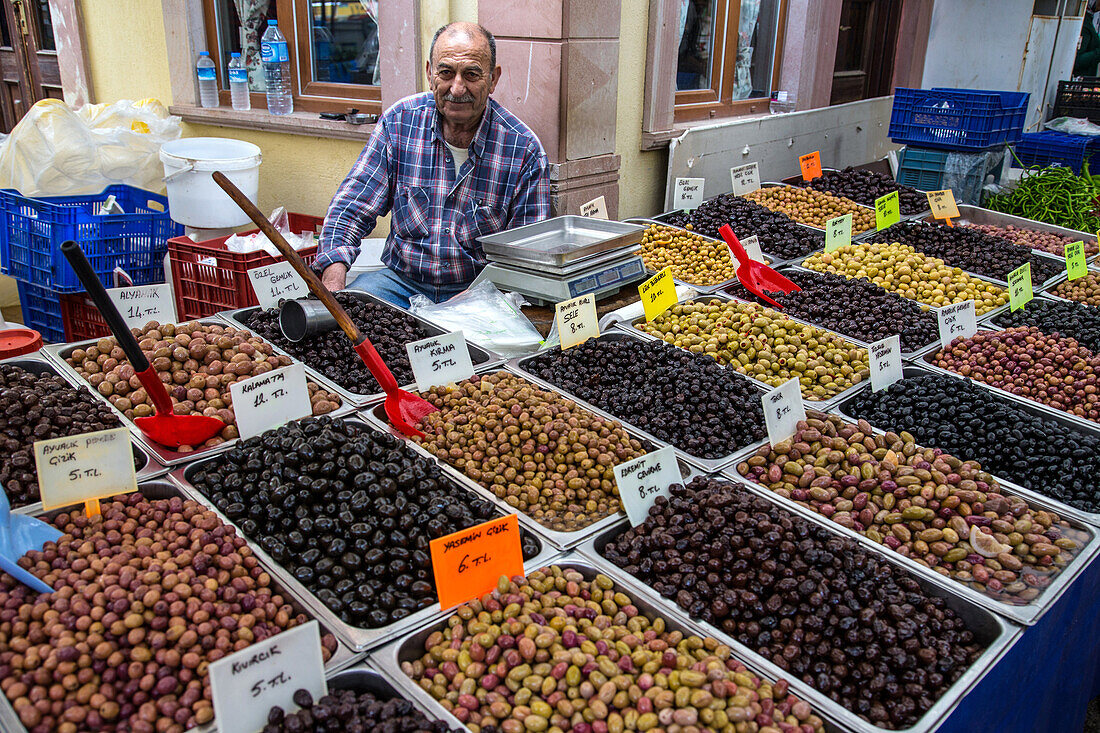 vendor in front of his olive stall, food market of namik kemal, cunda alibey, the olive riviera, north of izmir, turkey