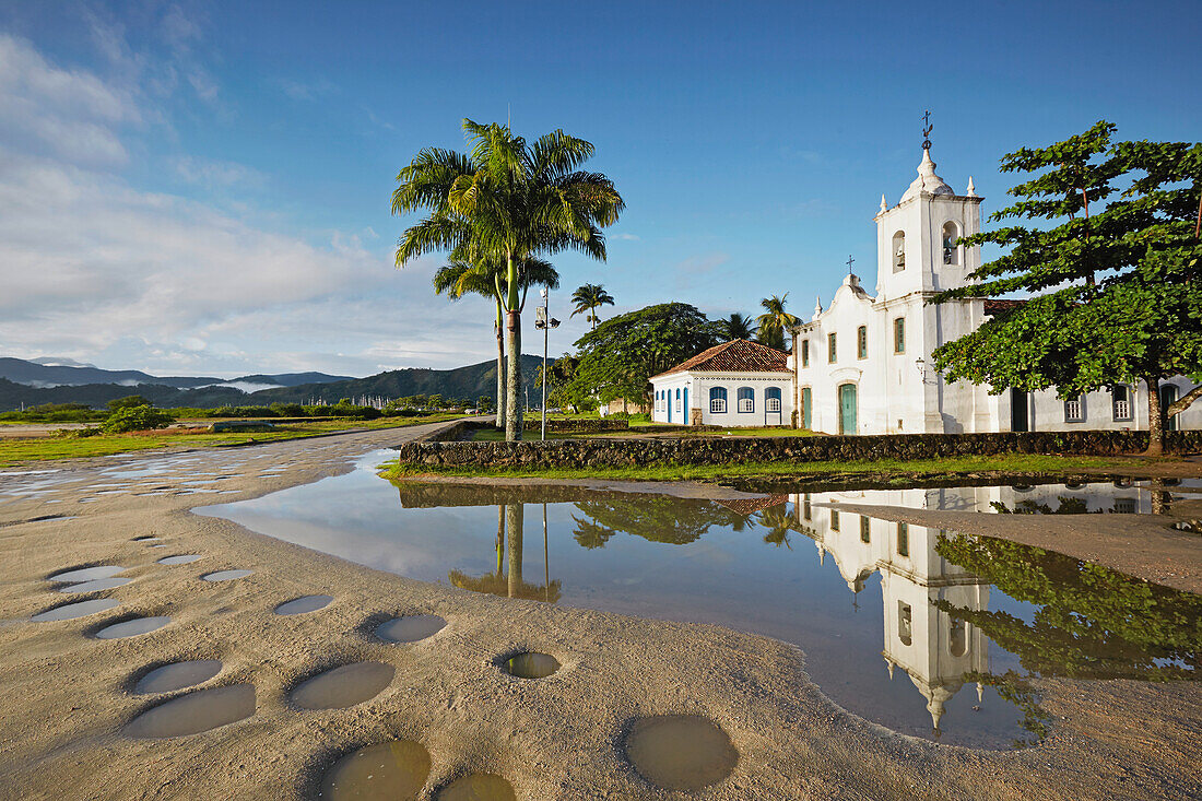 Morning sun, potholes, in the rain filled Rua Fresca, church Iglesia de Nostra Senora das Dores, historic old town, Paraty, Costa Verde, Rio de Janeiro, Brazil