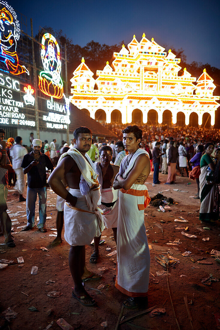 Men in traditional white Doti, illuminated timber scaffolding Aana Pandal in the back, Nemmara Vela, Vela Festival takes place in summer after harvest, Hindu temple festival in the village Nemmara near Pallakad, Kerala, India