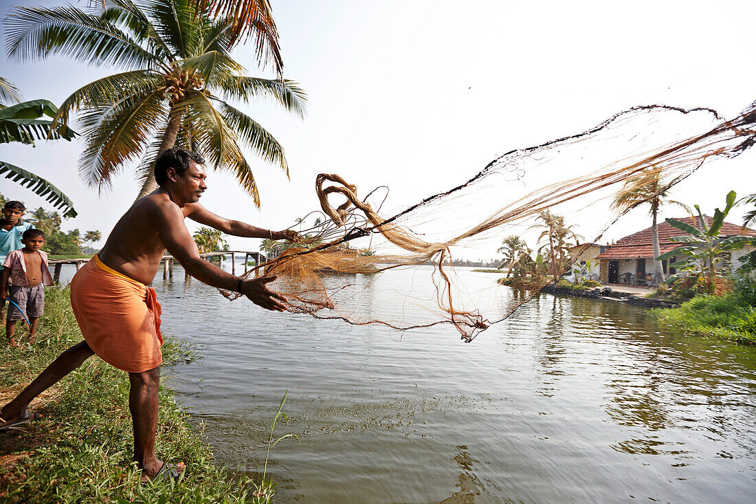 Sajeew ist Fischer und Bauer, wirft sein Fischnetz (Vishiwala), dahinter seine Soehne, auf kleinen Inseln in den Backwaters, Dorf Kainakarey, suedoestlich Aleppey, Backwaters, Kerala, Indien