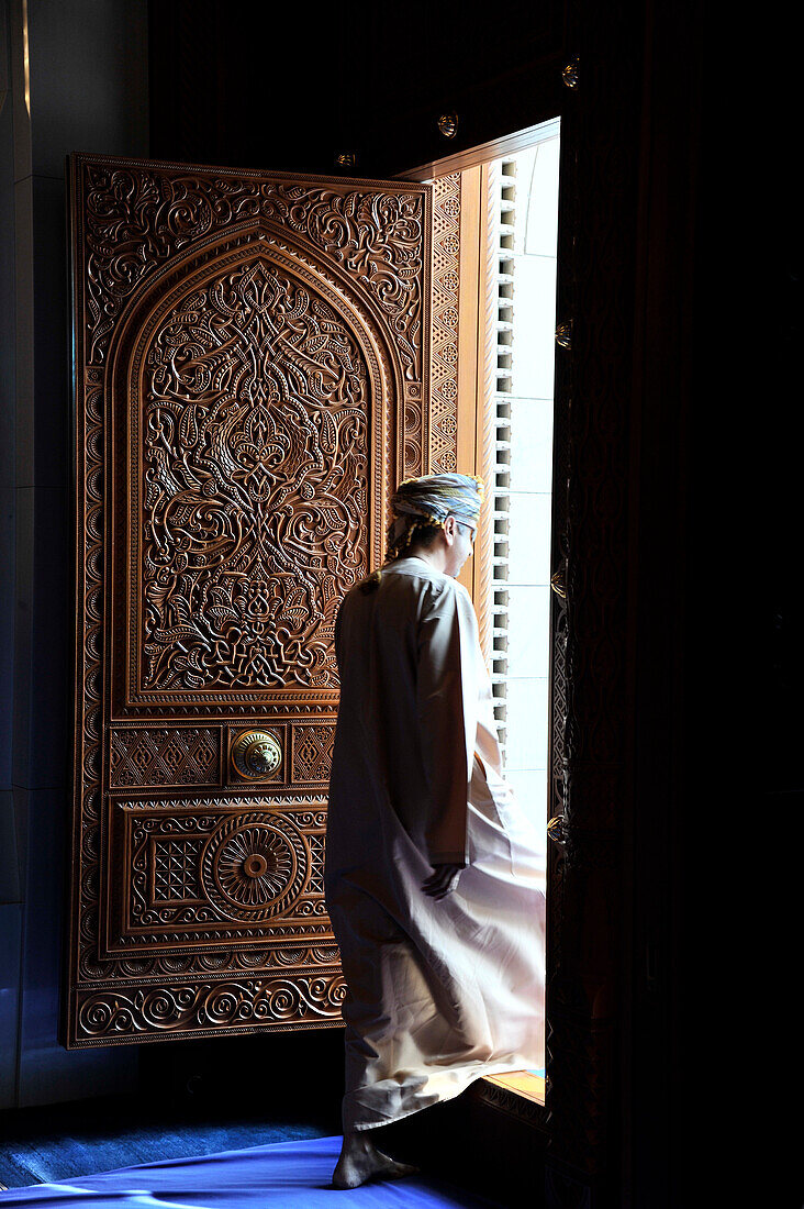 'Sultanate of OMAN, Muscat; Sultan qaboos mosque, a man wearing the traditional dishdasha  is passing in front of a sculpted wooden door'