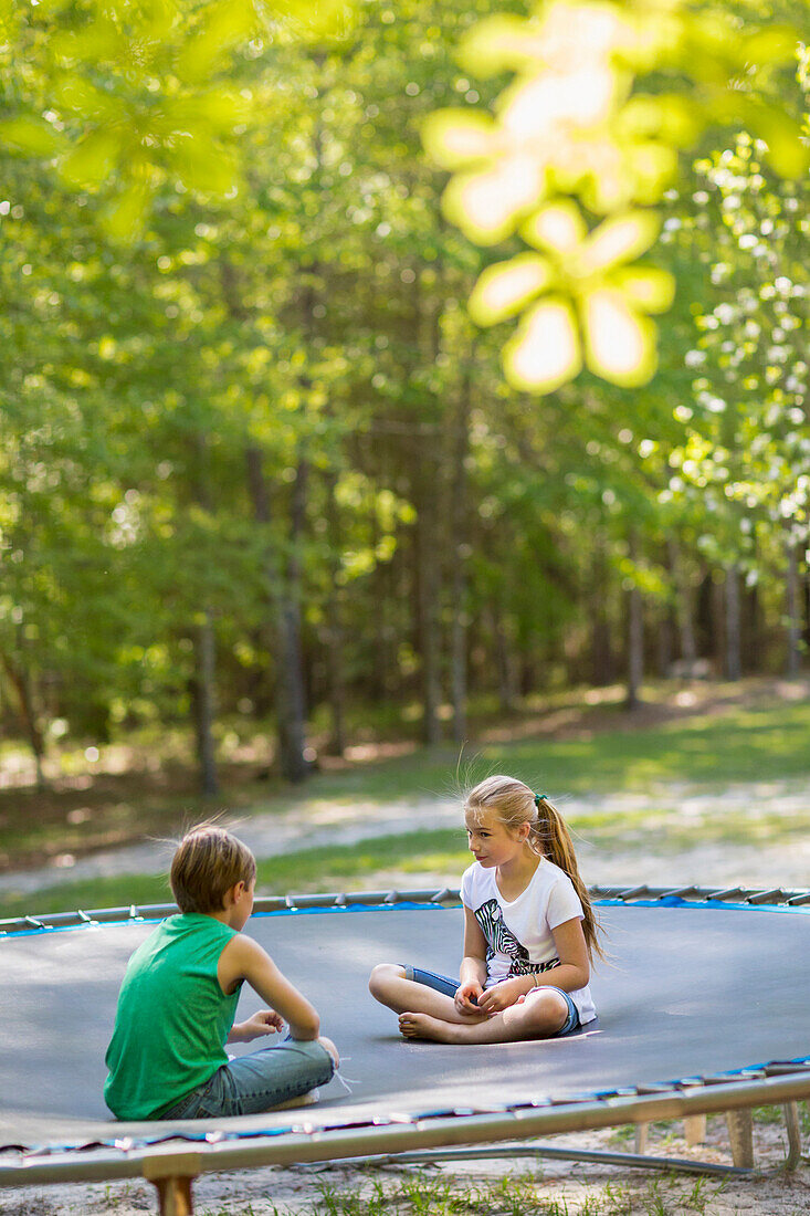 Caucasian children sitting on trampoline