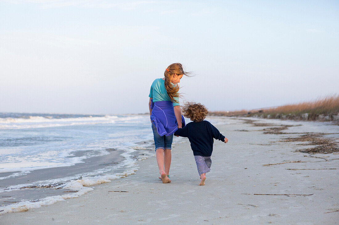 Caucasian brother and sister walking on beach