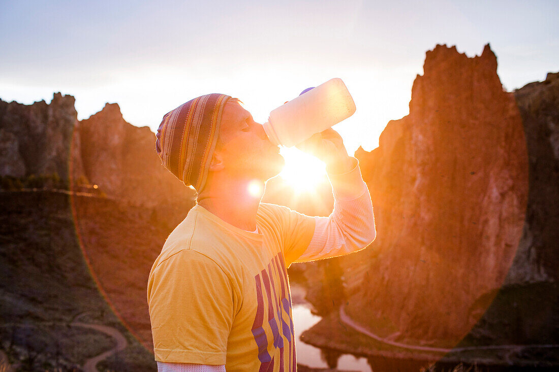 Caucasian man drinking water bottle in desert landscape, Smith Rock State Park, Oregon, United States