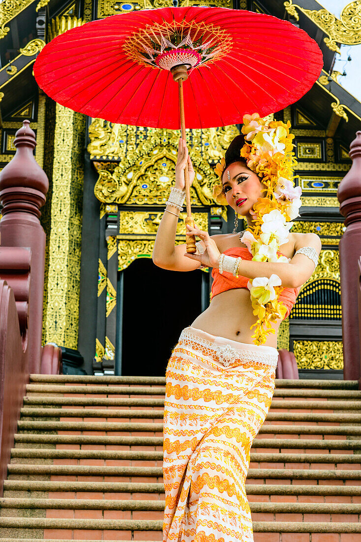 Asian woman with parasol on stairs of ornate Buddhist temple, Chiang Mai, Chiang Mai, Thailand