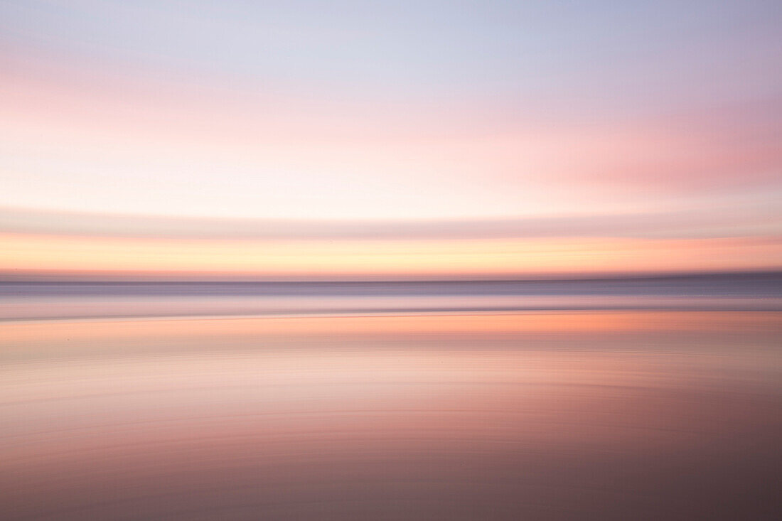 Defocused view of ocean waves on beach under sunset sky