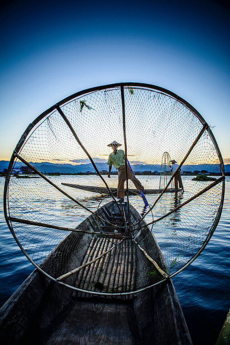 Asian fisherman using fishing net in canoe on river