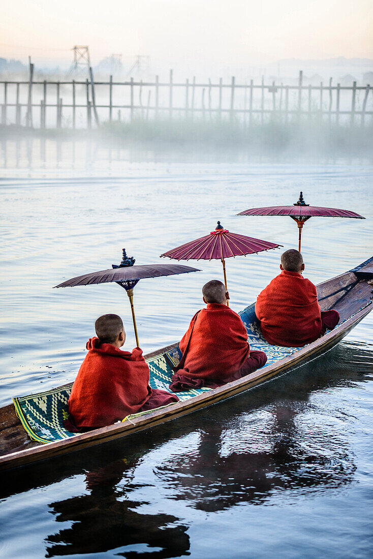 Asian monks under parasols in canoe on river