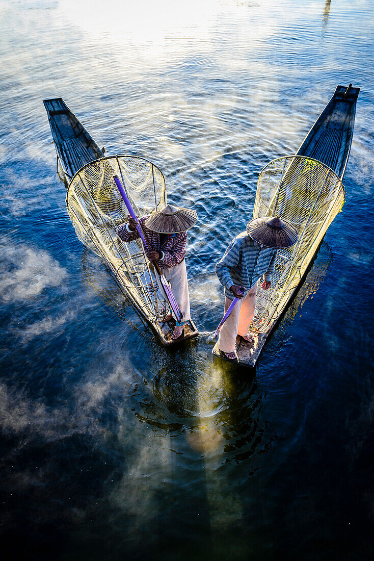 High angle view of Asian fishermen using fishing nets in canoe on river