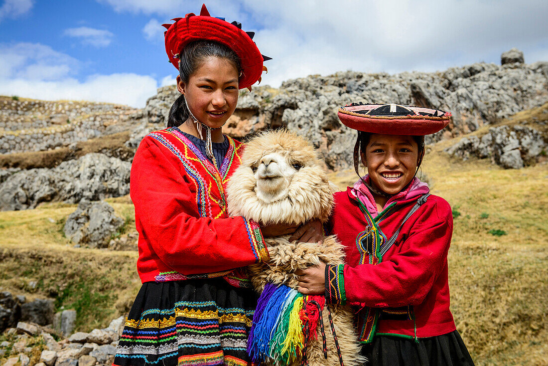 Hispanic sisters smiling with llama in rural landscape