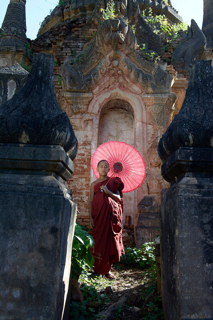 Asian monk-in-training with parasol walking on Buddhist shrine