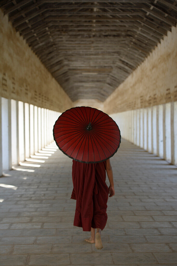 Asian monk-in-training carrying parasol in hallway
