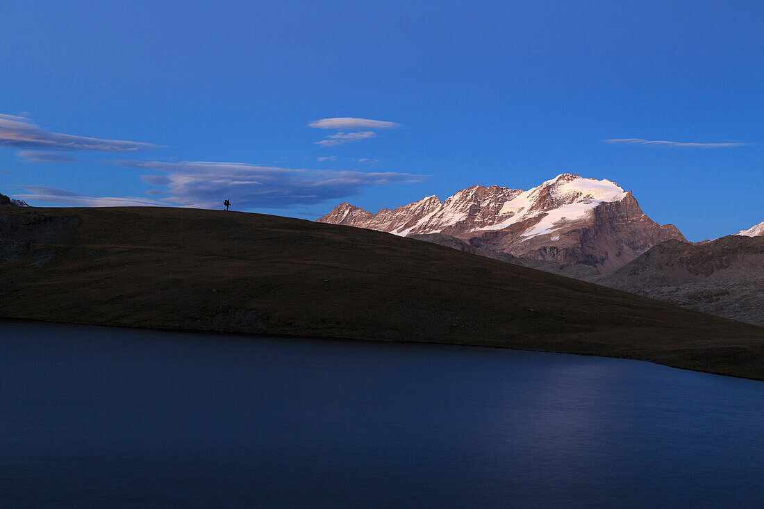 Hiker admires sunset on Rossett Lake at an altitude of 2709 meters, Gran Paradiso National Park, Alpi Graie (Graian Alps), Italy, Europe