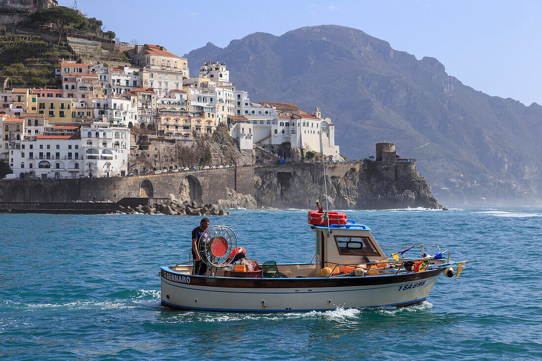 Fisherman in fishing boat heads out to sea from Amalfi harbour, with view towards Amalfi town, Costiera Amalfitana (Amalfi Coast), UNESCO World Heritage Site, Campania, Italy, Europe
