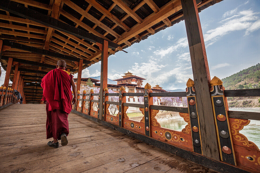 A monk (lama) of Punakha Dzong crosses the wooden bridge over the river that provides access to the ancient monastery, Bhutan, Asia