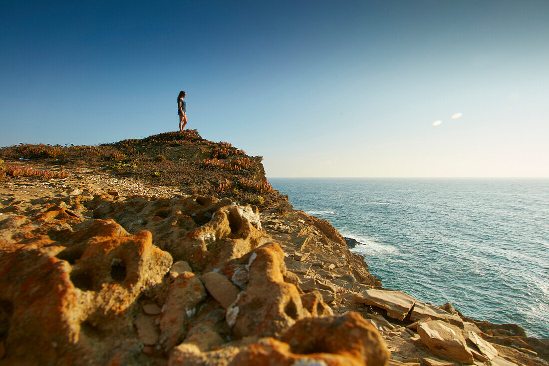 Young girl standing on the steep coast looking out to sea, Portugal