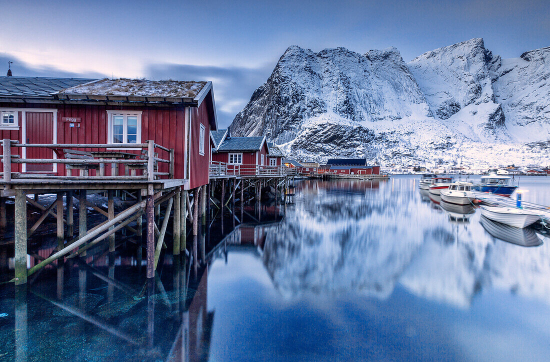 Snowy mountains and the typical red houses reflected in the cold sea at dusk, Reine, Lofoten Islands, Arctic, Norway, Scandinavia, Europe