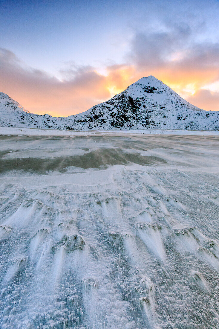 Wave advances towards the shore of the beach surrounded by snowy peaks at dawn, Uttakleiv, Lofoten Islands, Arctic, Norway, Scandinavia, Europe