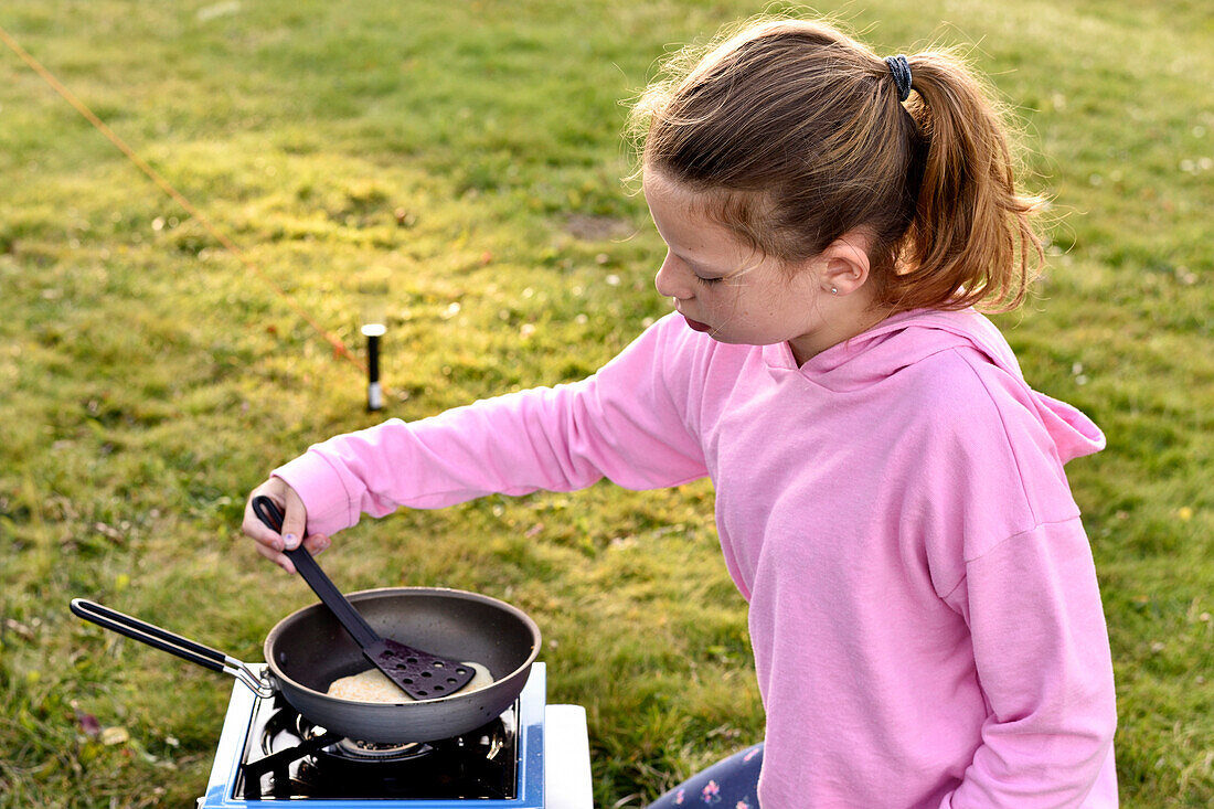 Mädchen brät draußen Pfannkuchen, Campingplatz, Västervik, Smaland, Schweden