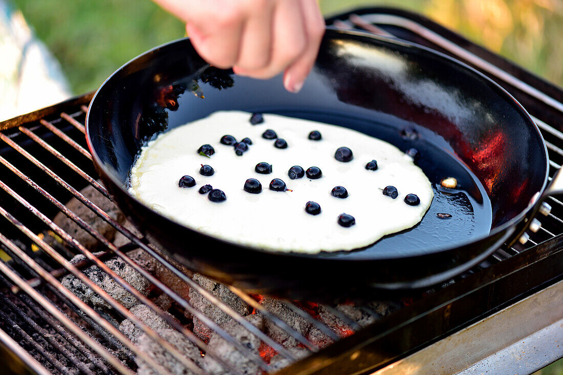 Pan on top of charcoal grill with blueberry pancakes, camping ground, Vaestervik, Smaland, Sweden
