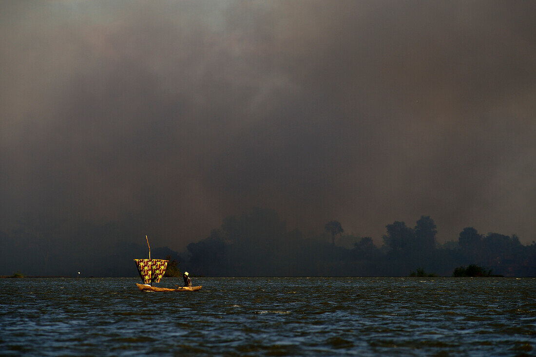 Einbaum-Segelboot mit Waldbrand im Hintergrund, Selous Natur Reservat, Tansania, Afrika