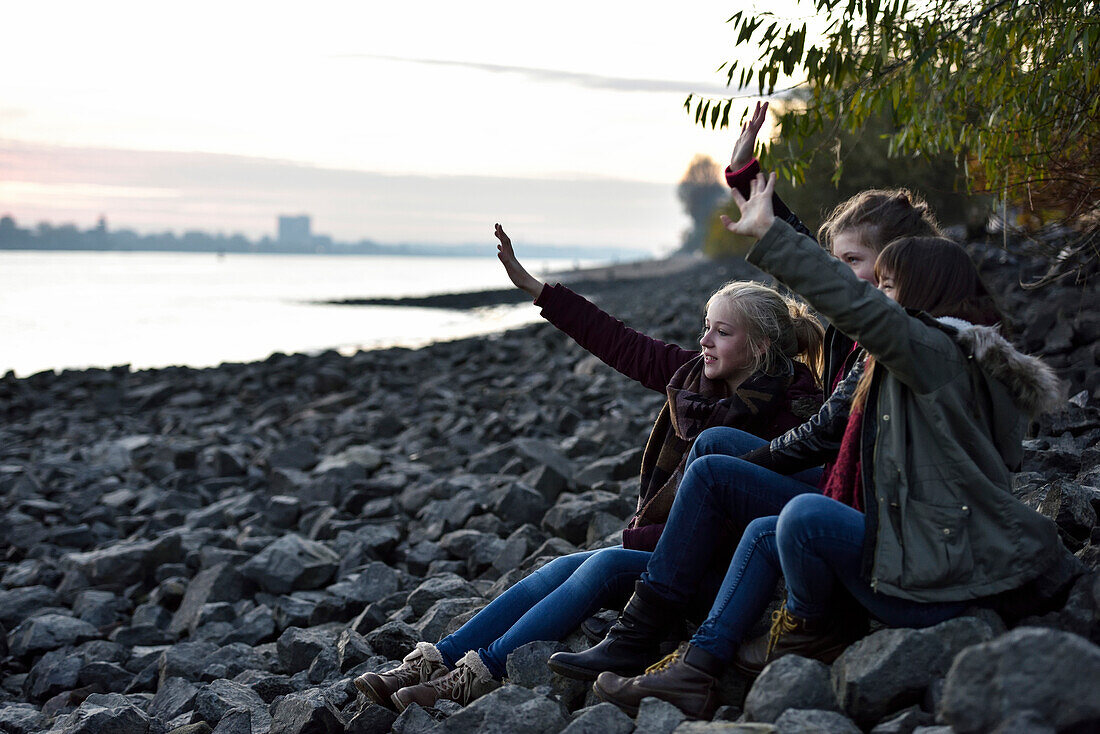 3 girls looking towards the port and waving, Elbe River beach, Oevelgoenne, Hamburg, Germany, Europe