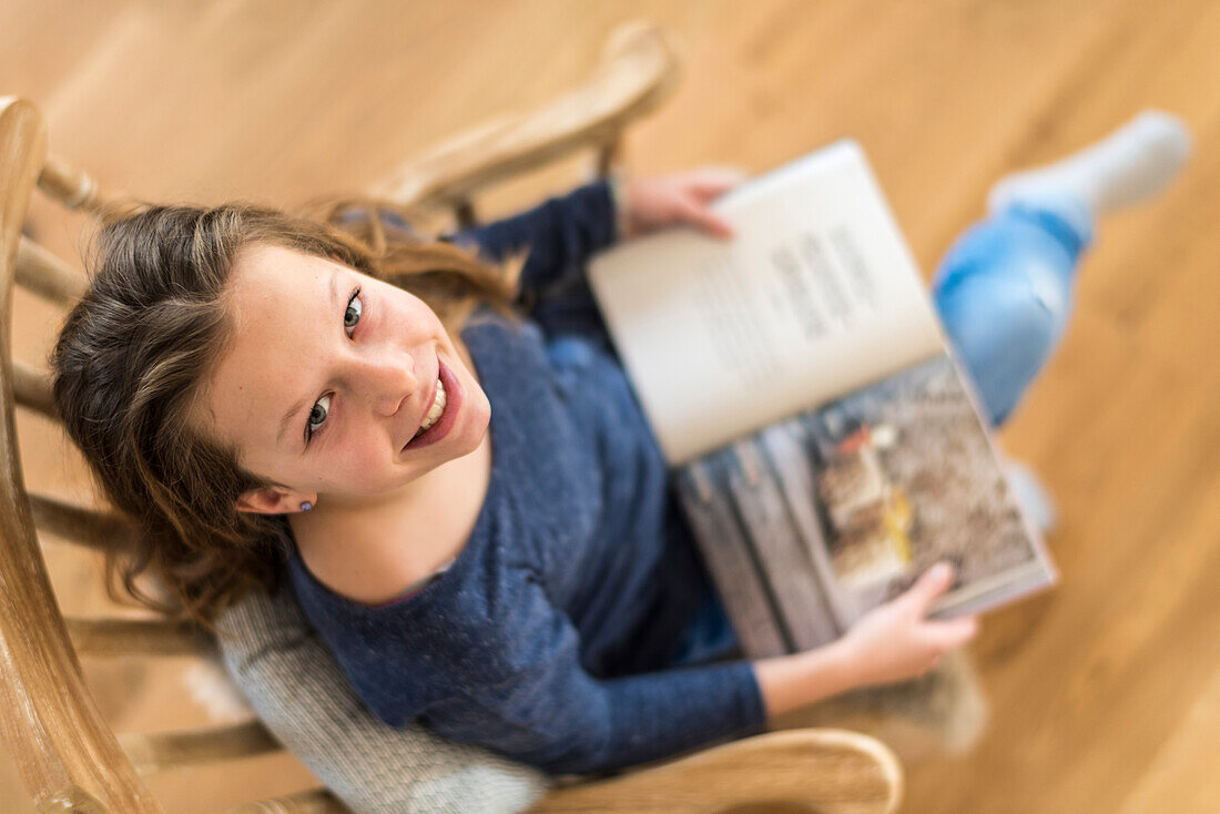 Mädchen liest auf dem Schaukelstuhl im Wohnzimmer, Hamburg, Deutschland, Europa