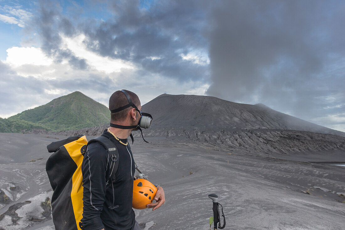 Eruption of the active Tavurvur volcano and ash cloud. Man with gas mask and helmet in the front, the green cone of the „Vulcan'' volcano in the background, New Guinea, New Britain, South Pacific