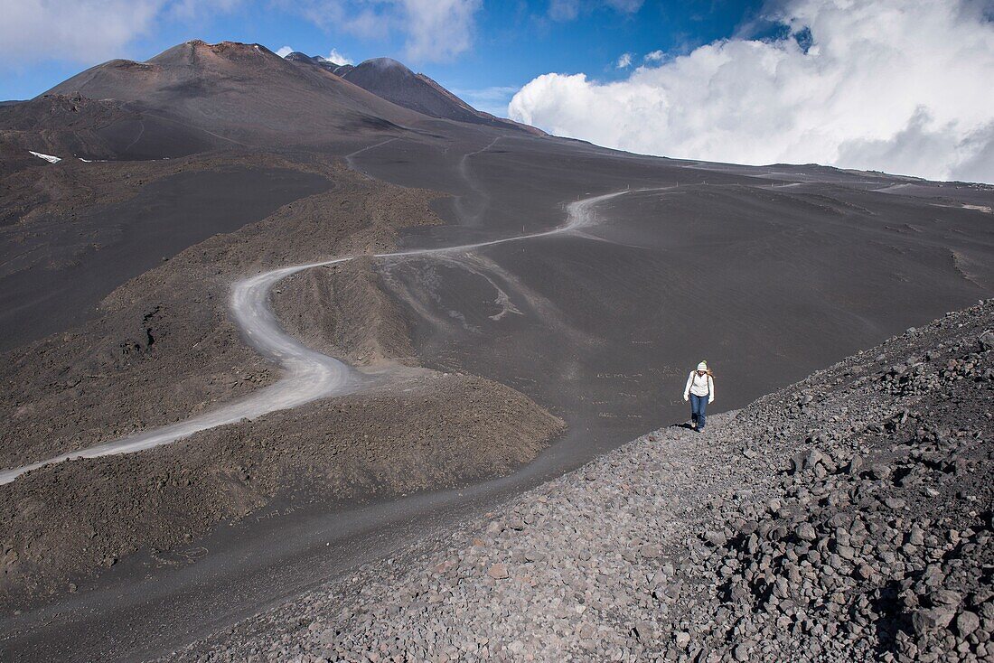 Large ash field with car tracks at the foot of the Etna in about 3000m altitude. Woman walking through the ash field, Sicilian, Italy