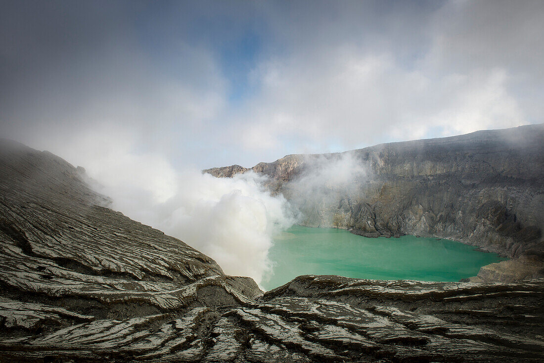 View over the crater rim consisting of ash an on the turquoise blue acid lake of Ijen volcano. Ash washed out by precipitation, gases emitting, East Java, Ijen volcano, Indonesia