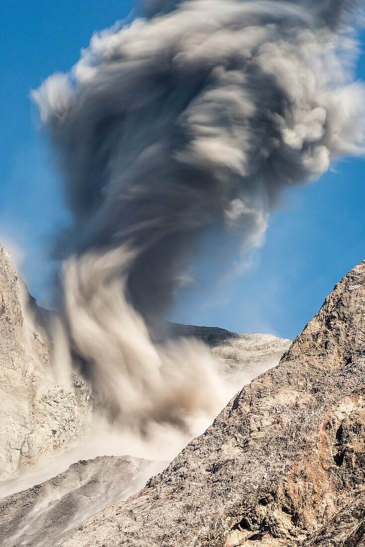 Langzeitbelichtung einer großen Asche-Eruption und Gesteinsauswurf an der offenen Flanke des Vulkans Batu Tara in der Flores Sea bei Tage vor blauem Himmel mit Vulkan-Gasen und Asche, Insel Komba, Flores Sea, Indonesien